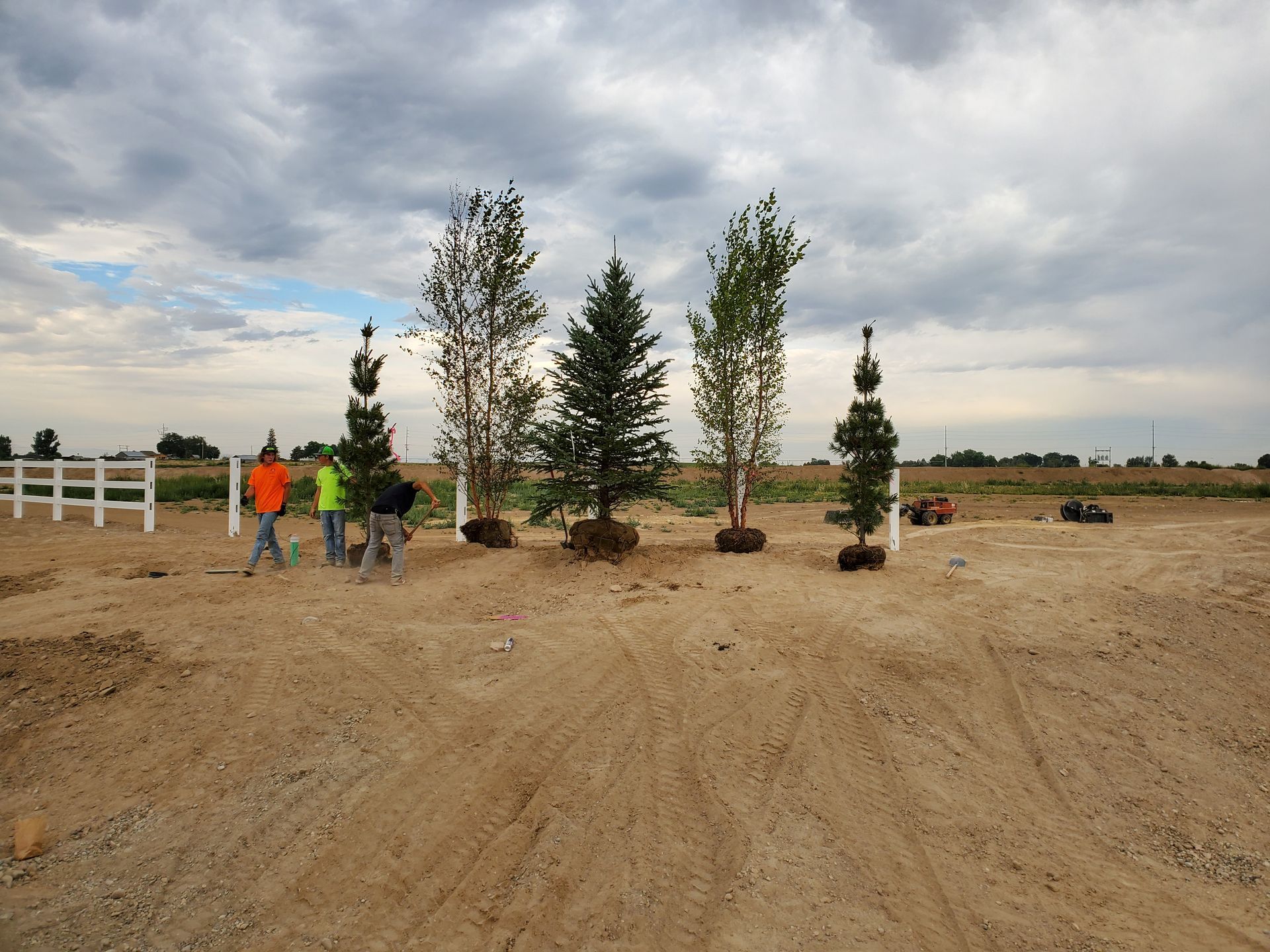A group of people standing in a dirt field with trees in the background