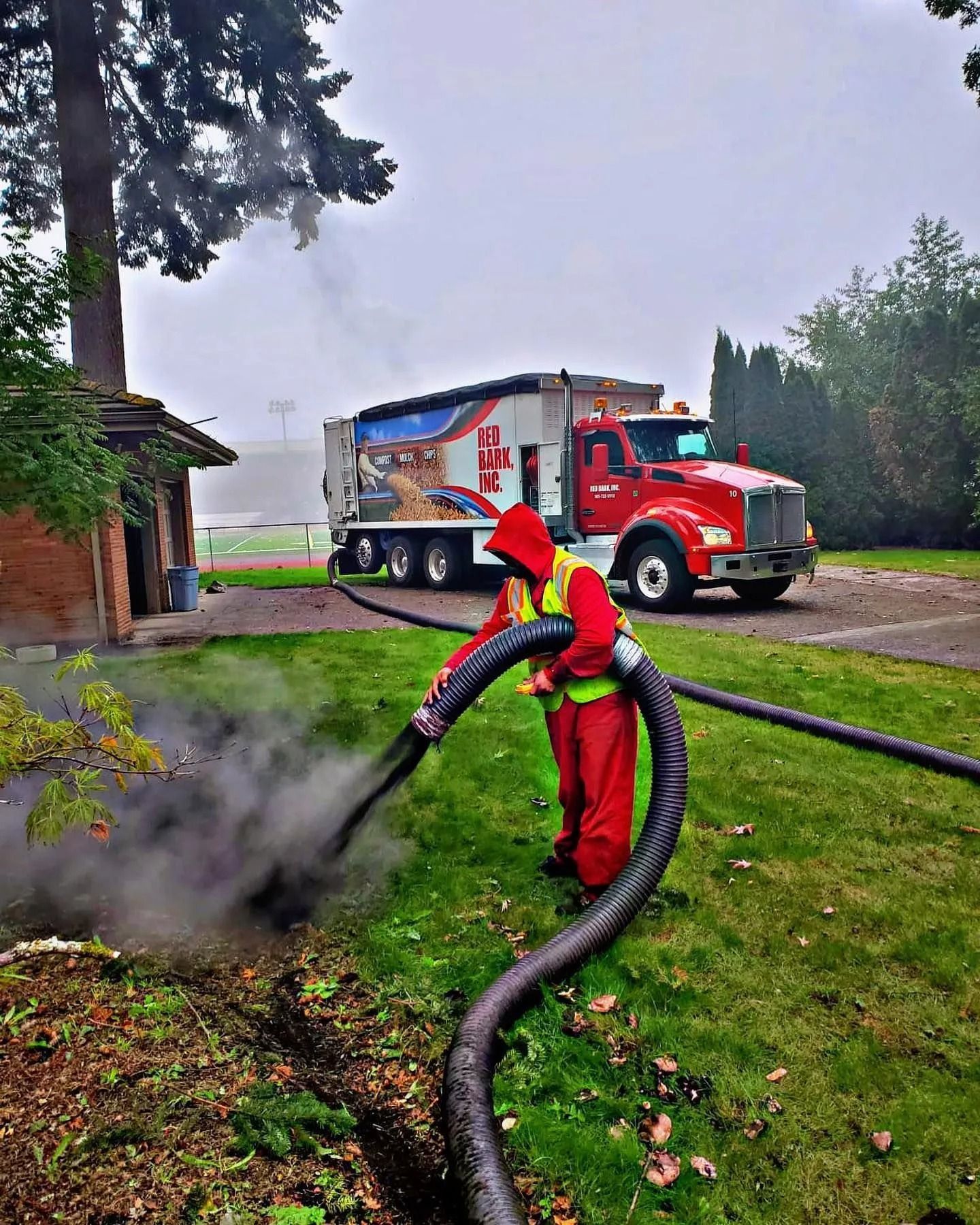 Person in red suit operates hose, dark smoke rises. Red truck in background, green grass.