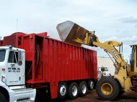 Yellow loader dumping material into a red truck trailer. The truck says 