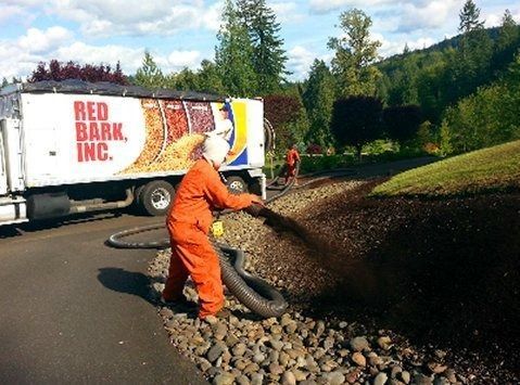 Workers in orange suits spraying mulch from a Red Bark truck onto a hillside.