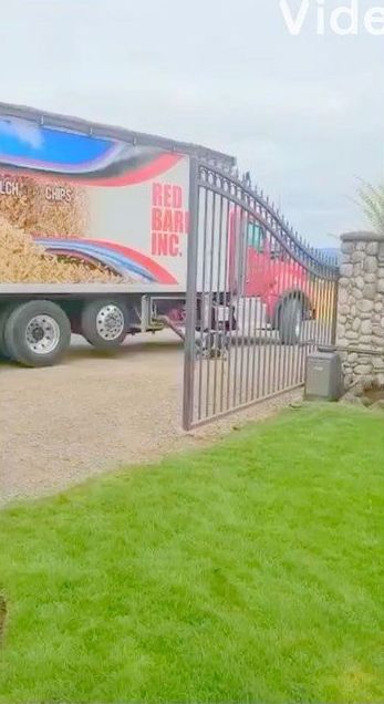Semi-truck with wood chips entering a property through a gated entrance.