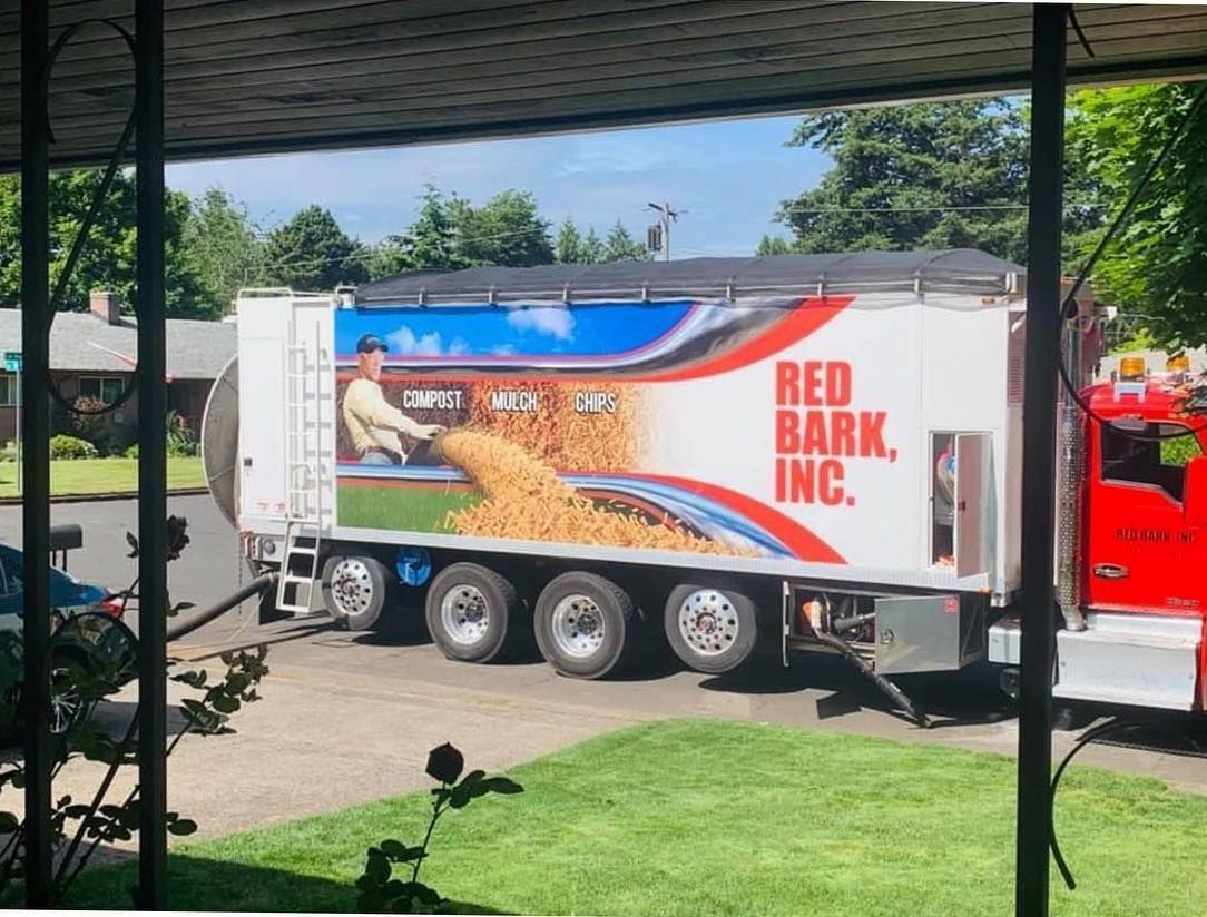 Red Bark Inc. truck delivering bark, side view. White truck with red branding, illustration of man spreading bark.