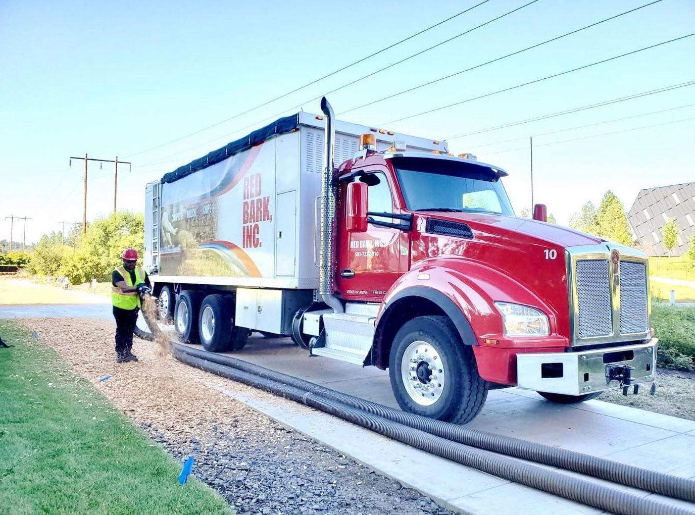 Red semi-truck with a worker, parked next to tubes. The truck has a covered cargo area. Sunny outdoor setting.