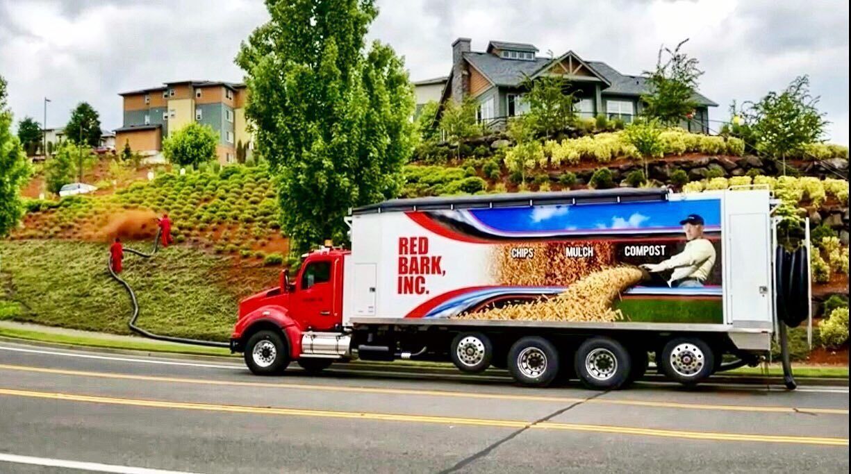 Red truck with Red Bank Inc. logo, graphic of man and potatoes, parked next to a hillside and houses.