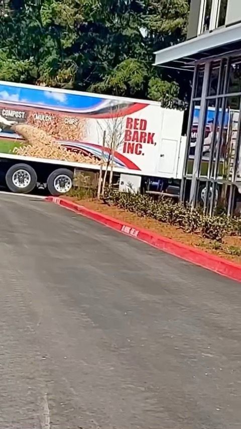 Red Bark Inc. truck parked near a building. The truck is white with red lettering and is loaded with wood chips.