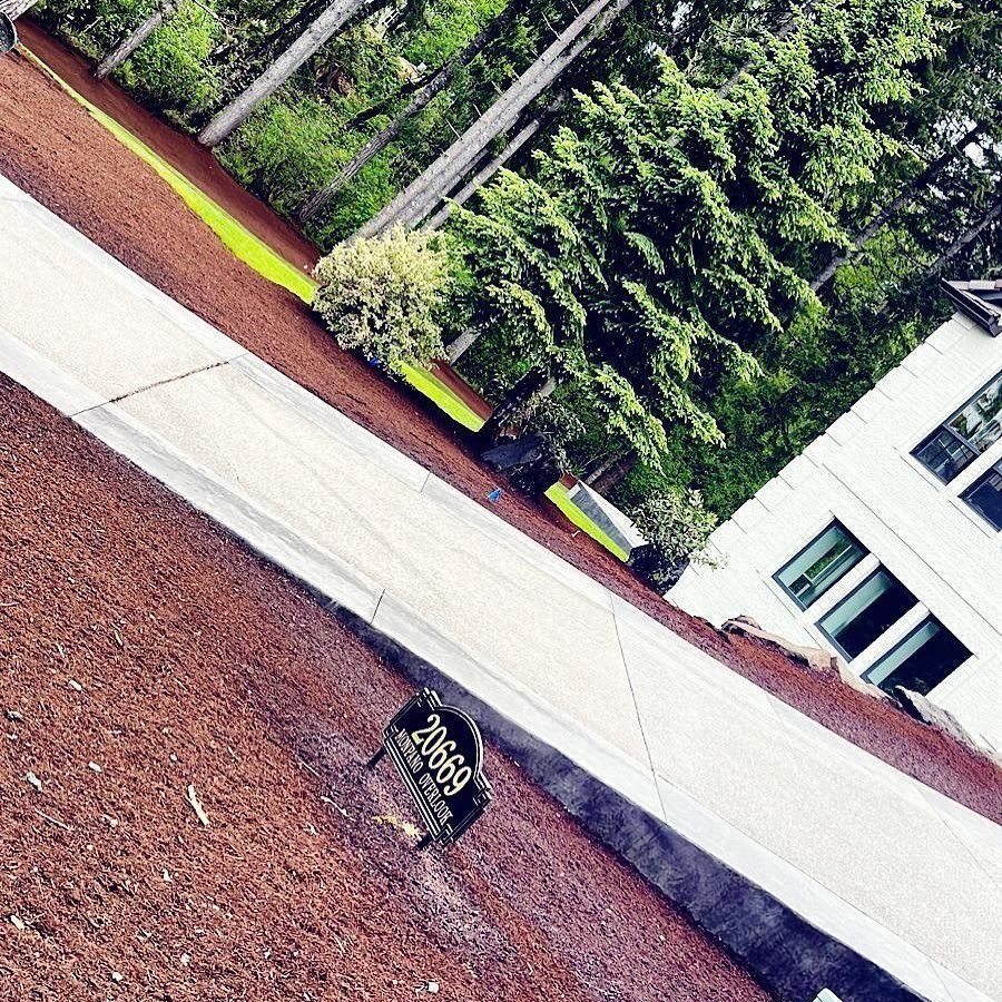 House number sign on a long driveway with red mulch, trees, and white house.