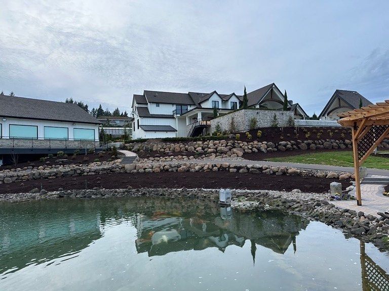 Lakeside view of a large, modern home with a white exterior under a cloudy sky. Reflective water in the foreground.