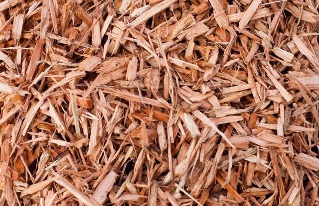 Reddish-brown wood chips scattered on a surface, likely for landscaping or gardening.