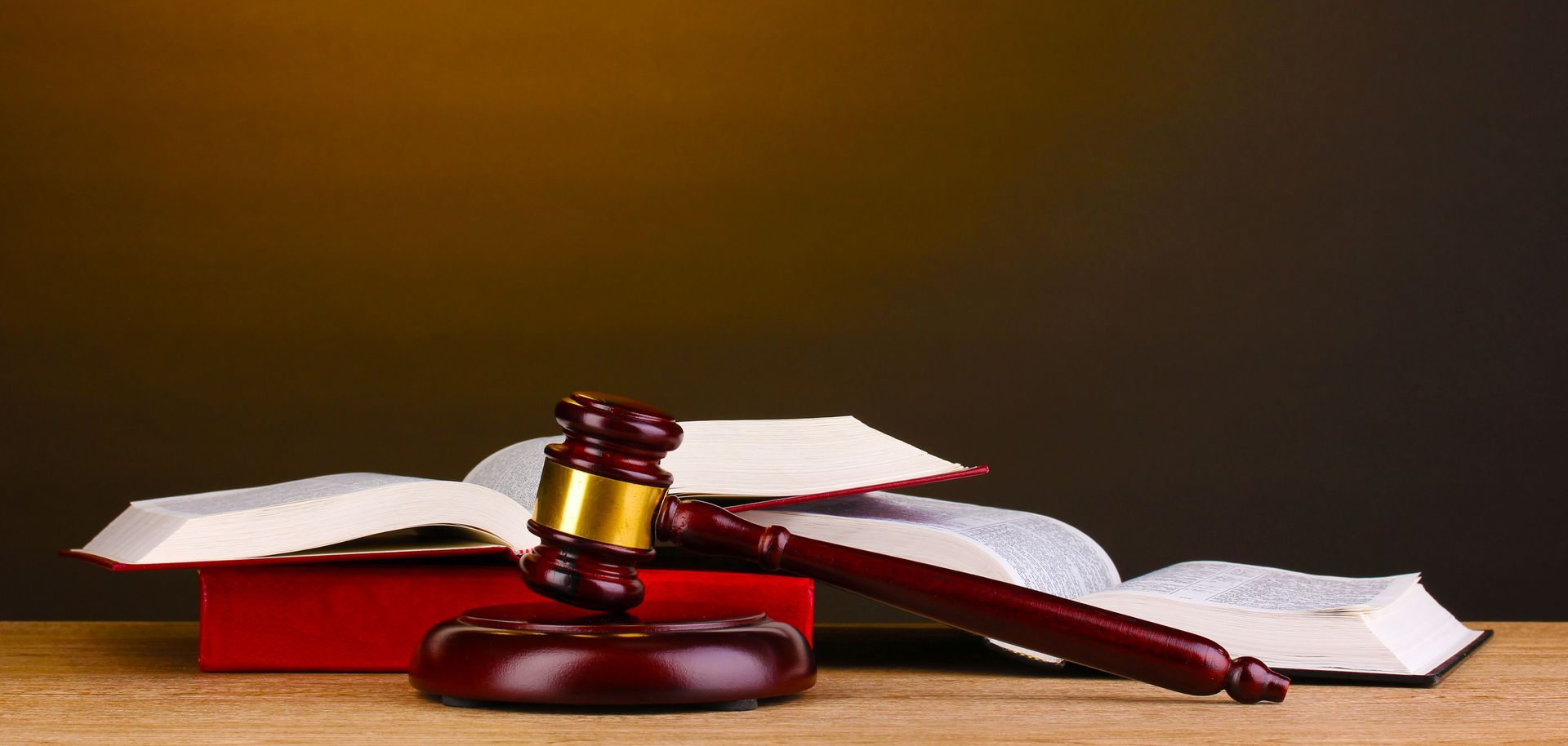 Gavel and books on a wooden surface against a dark background, symbolizing law and justice.