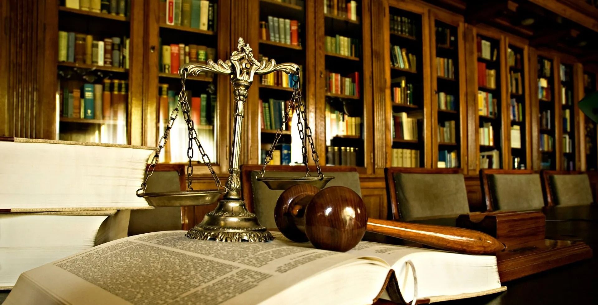 Scales of justice, books, gavel, and apples on a table in a library.