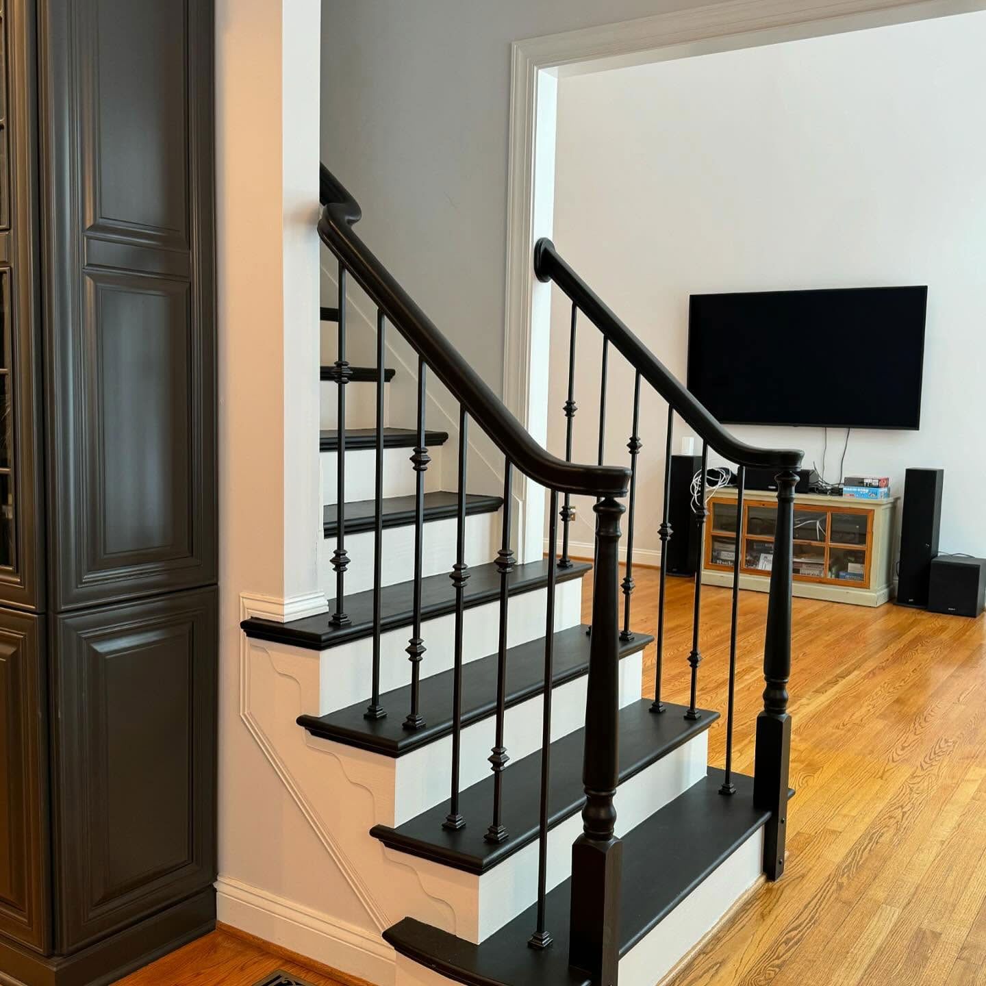 A staircase with dark wood treads and a black metal railing leads to a home interior with a wall-mounted TV.