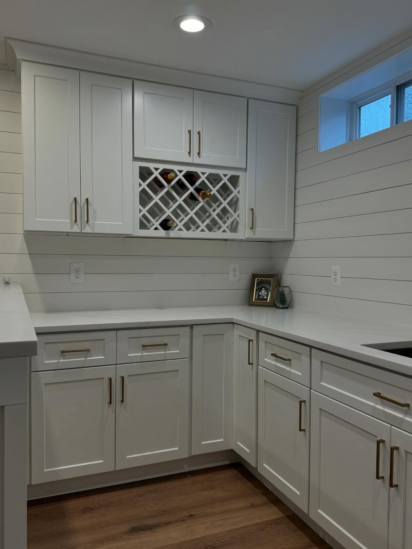 White kitchen cabinetry with a built-in wine rack and countertop set against white shiplap walls and wood flooring.