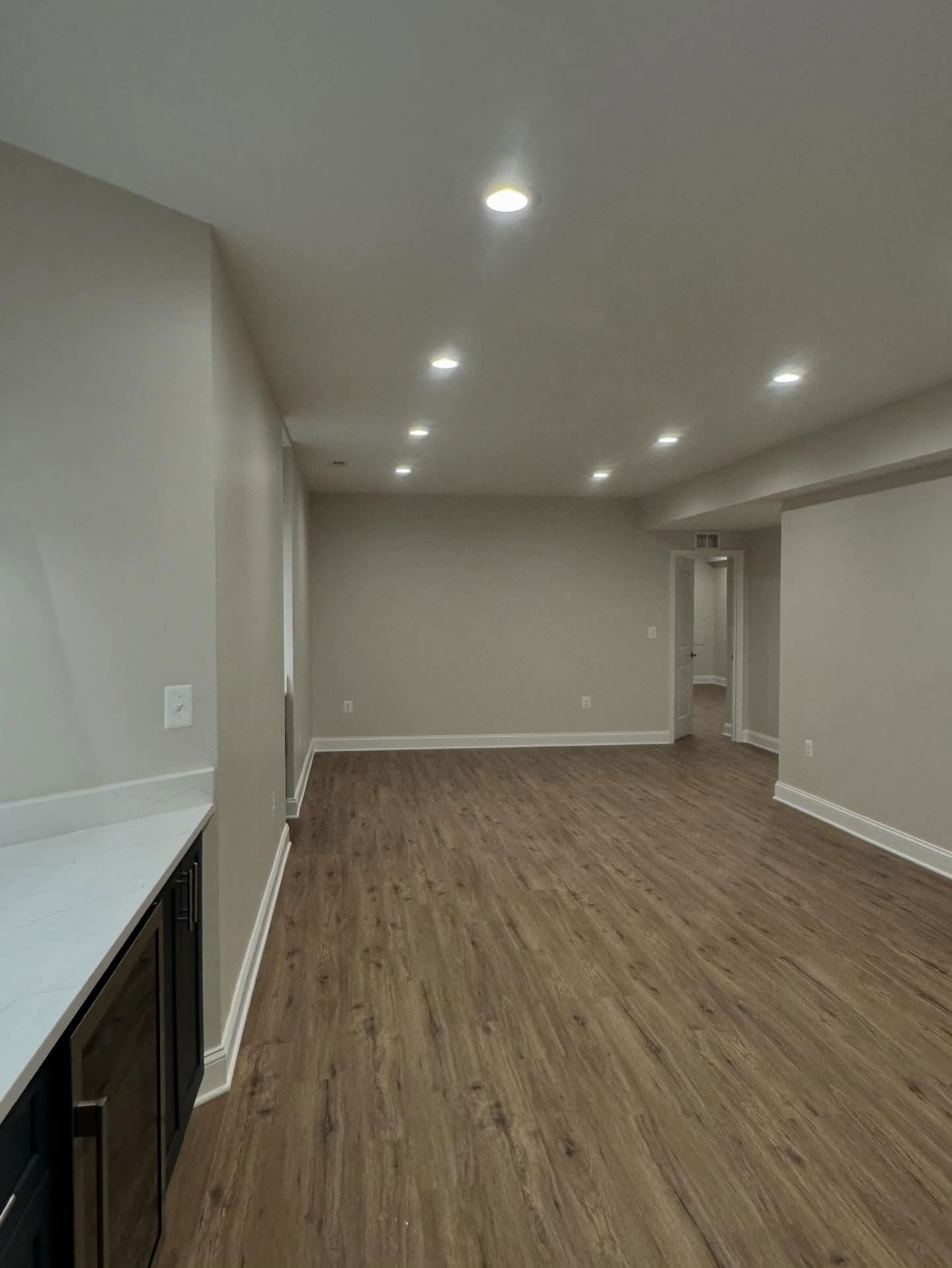 A wide-angle view of a modern, empty basement with neutral walls, recessed lighting, and wood-look flooring.