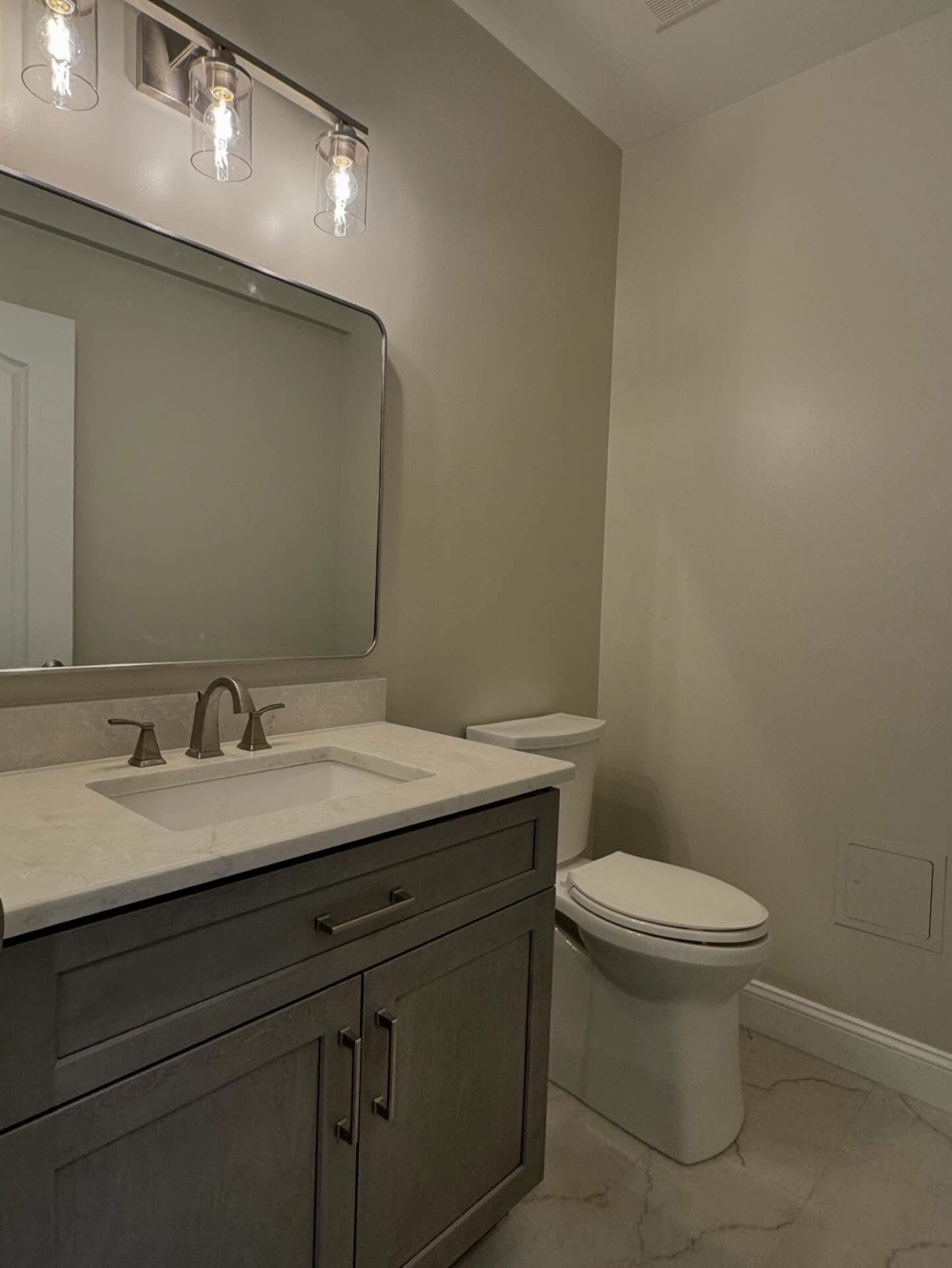 A modern bathroom featuring a gray vanity with a white countertop, a mirror, and a white toilet against light gray walls.