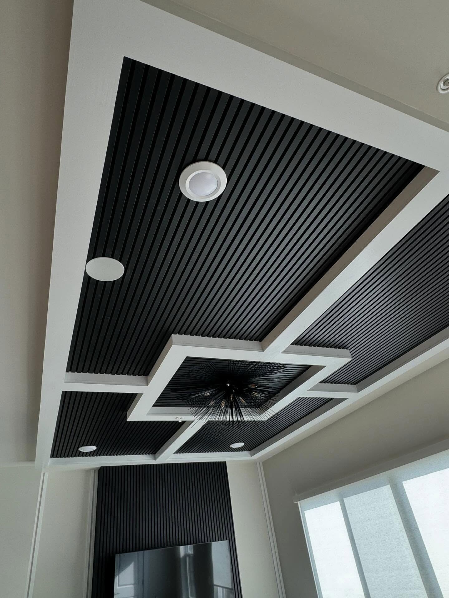 A modern tray ceiling with black fluted panels, white molding, recessed lights, and a central sputnik-style chandelier.