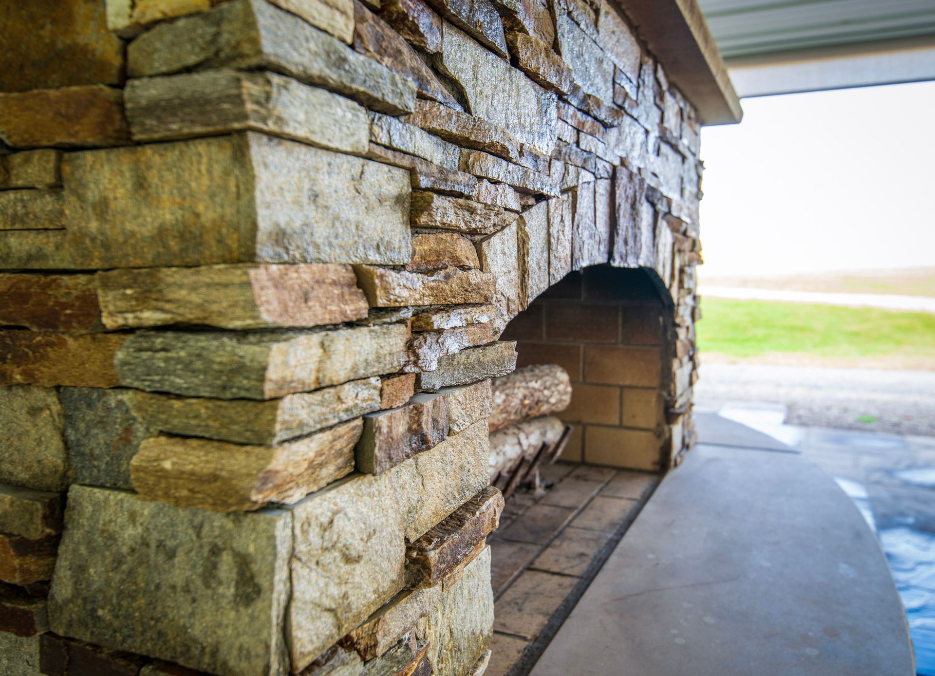 Stone fireplace with firewood inside, under a covered outdoor space.