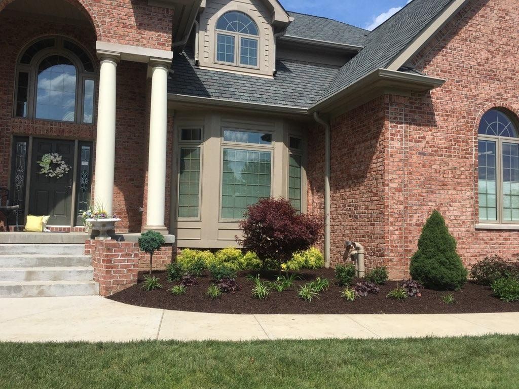 Brick house with landscaped front yard: flowers, shrubs, and a trimmed lawn.