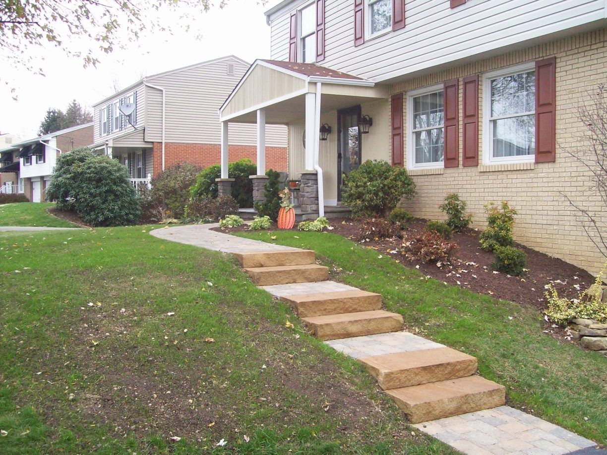 Stone steps lead up to a house with tan siding and red shutters; green lawn and porch.