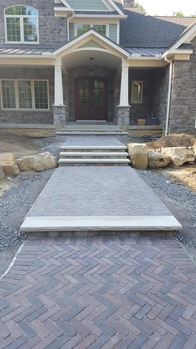 Brick walkway with herringbone pattern leading to a home's entrance with steps and stone facade.