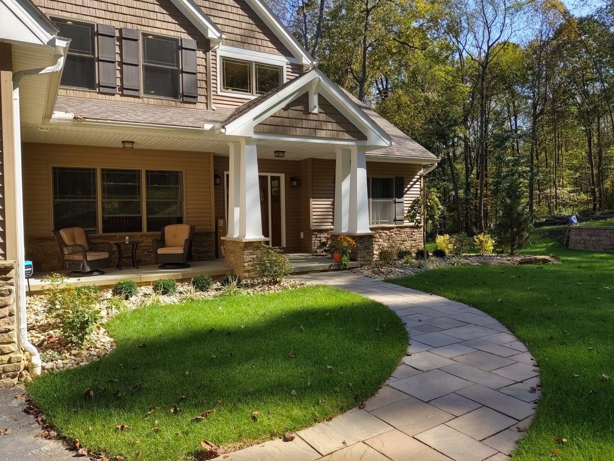 Stone pathway leads to a house with a porch and lawn.