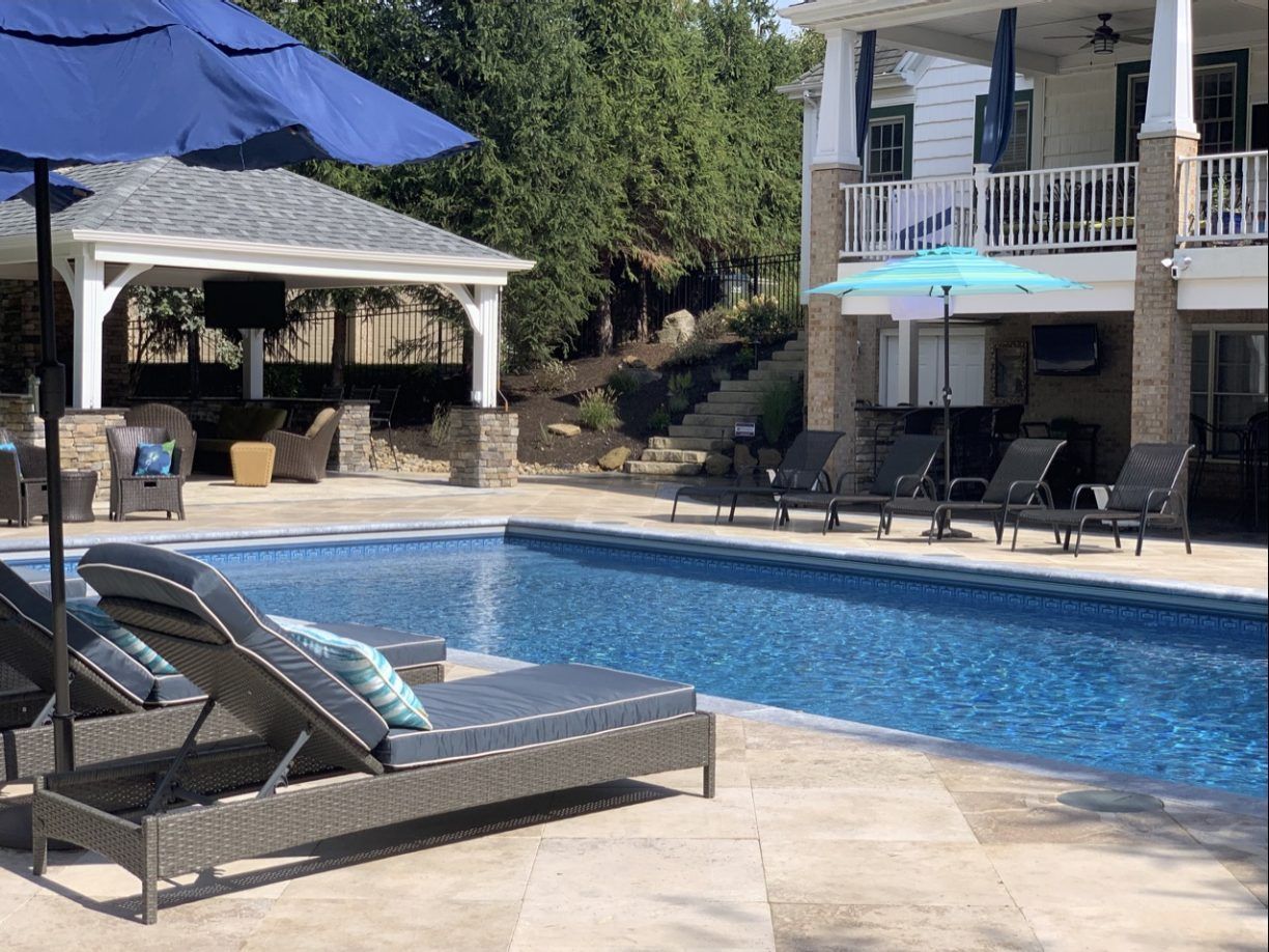 Poolside scene with a pool, lounge chairs, a gazebo, and a two-story house.