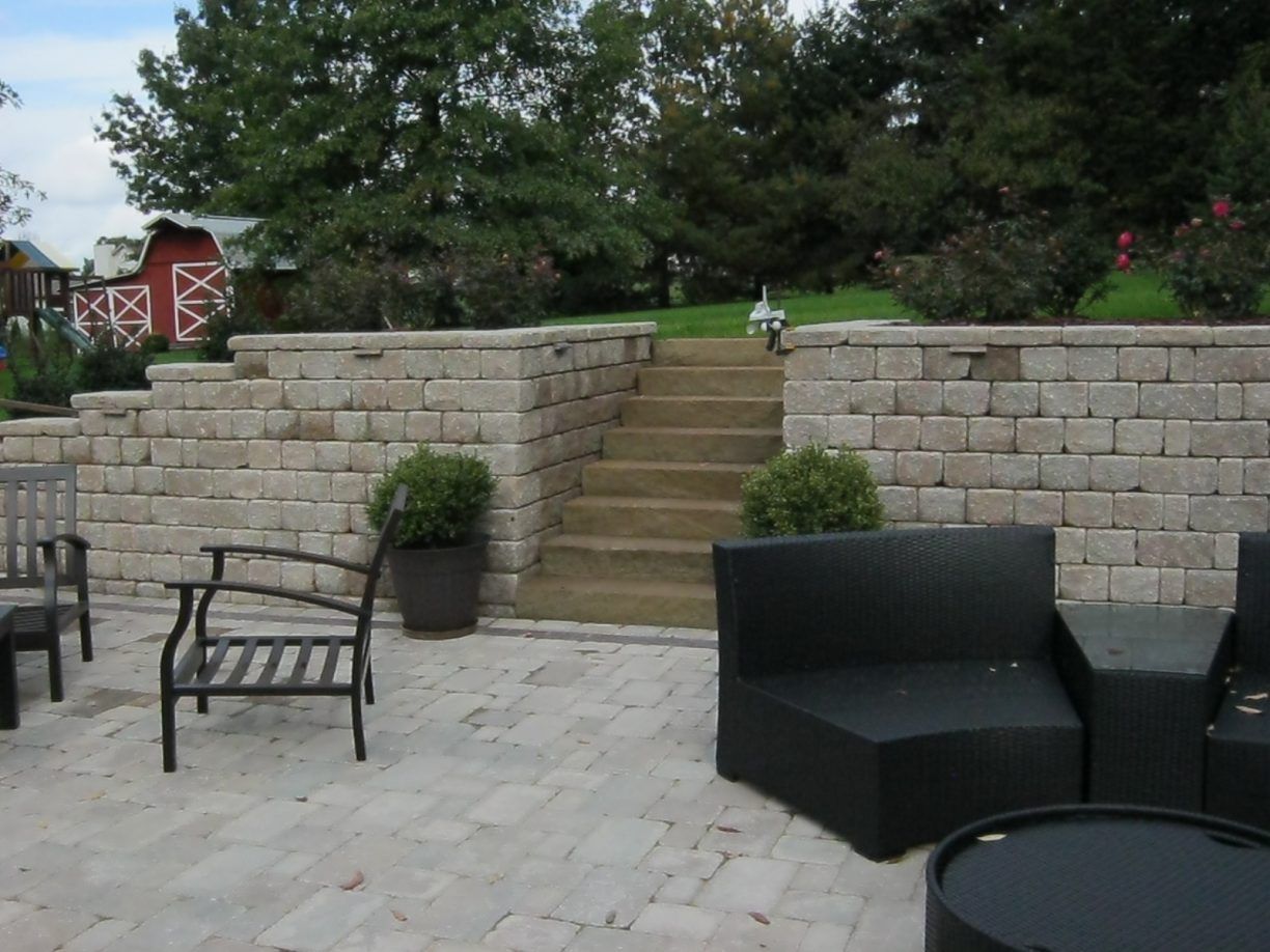 Stone patio with steps, retaining walls, and outdoor furniture. A red barn is in the background.
