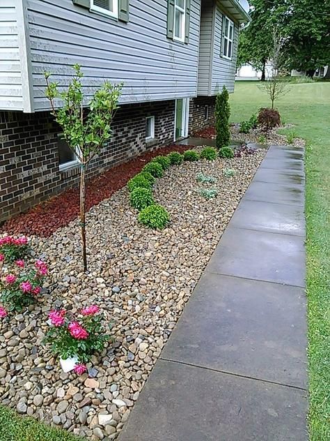 A house with a rock garden filled with plants and a sidewalk on its side.