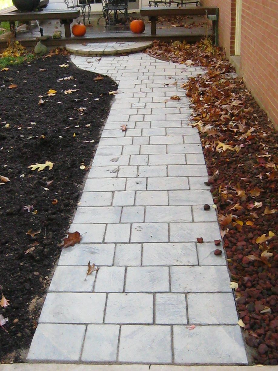 Stone walkway with fall leaves on either side, leading to a wooden deck with pumpkins.