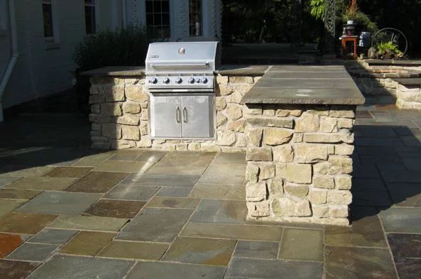 Outdoor kitchen with stainless steel grill, stone countertops, and flagstone patio.