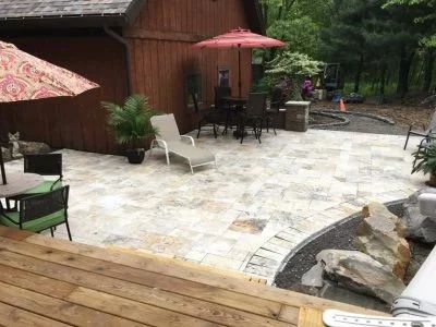 Patio with furniture, parasols, and plants next to a wooden structure and landscaping with a rock feature.