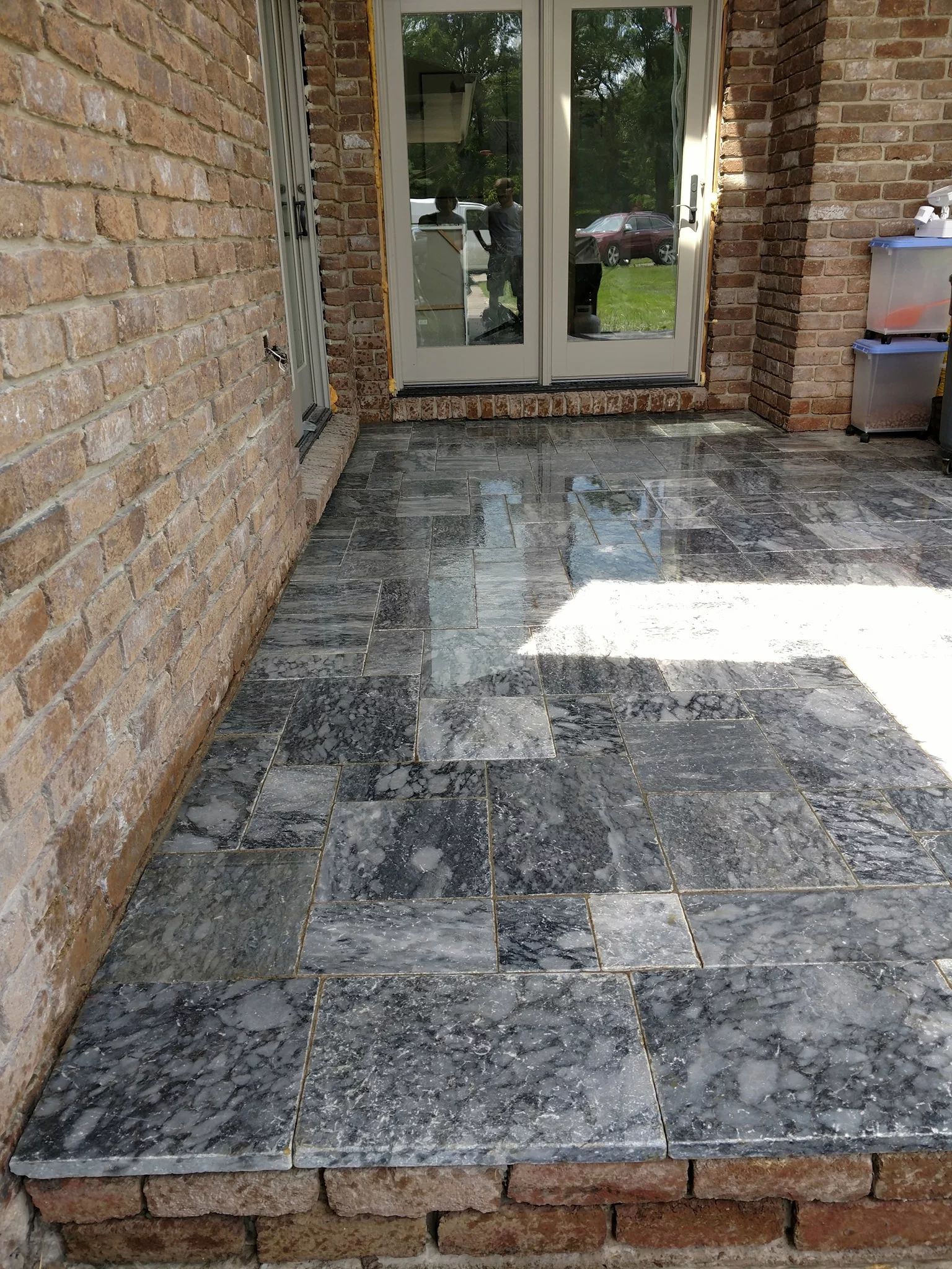 Brick patio with dark gray tiled floor, leading to glass French doors.