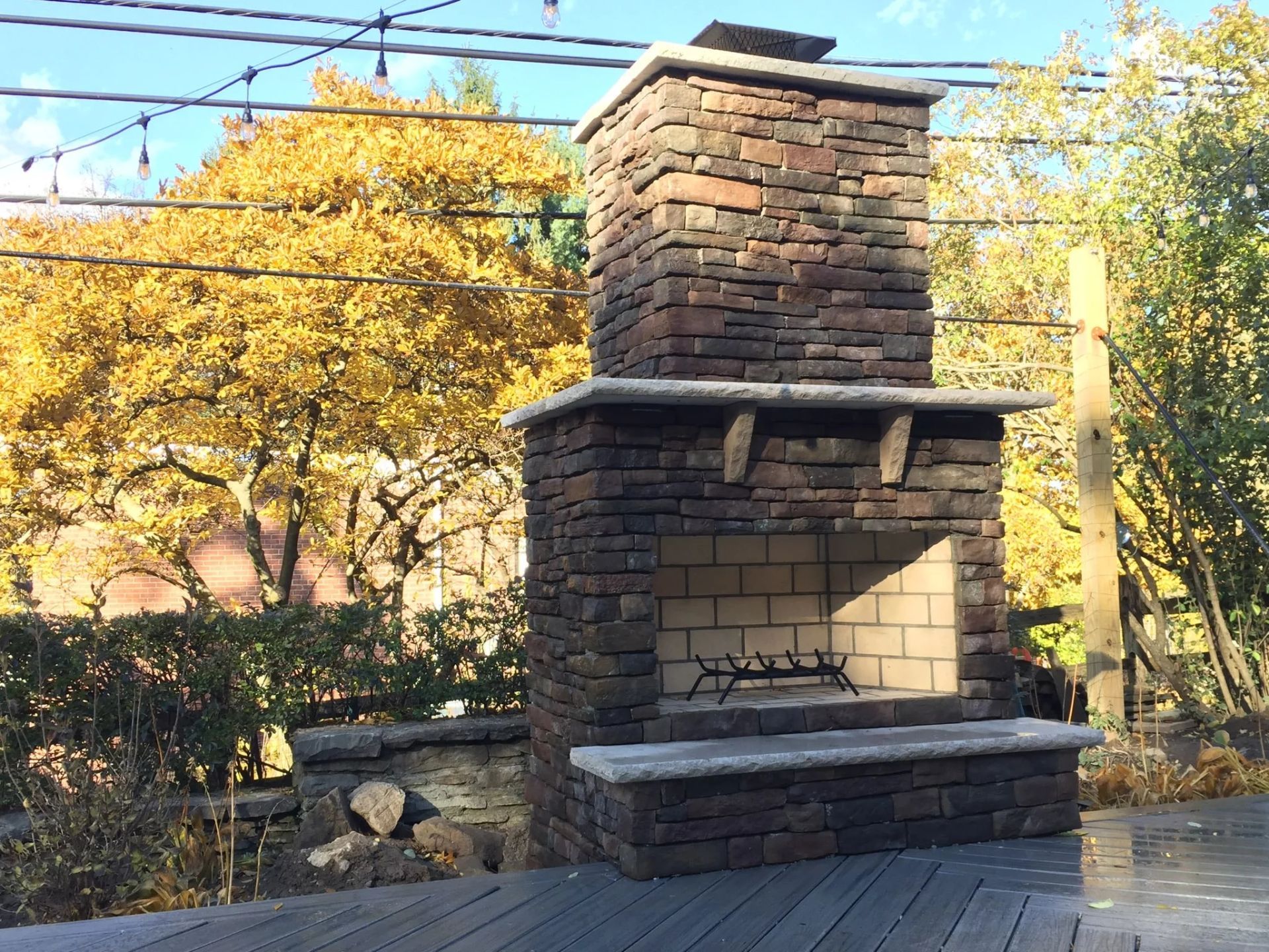 Stone outdoor fireplace with brick interior, autumn foliage in background.