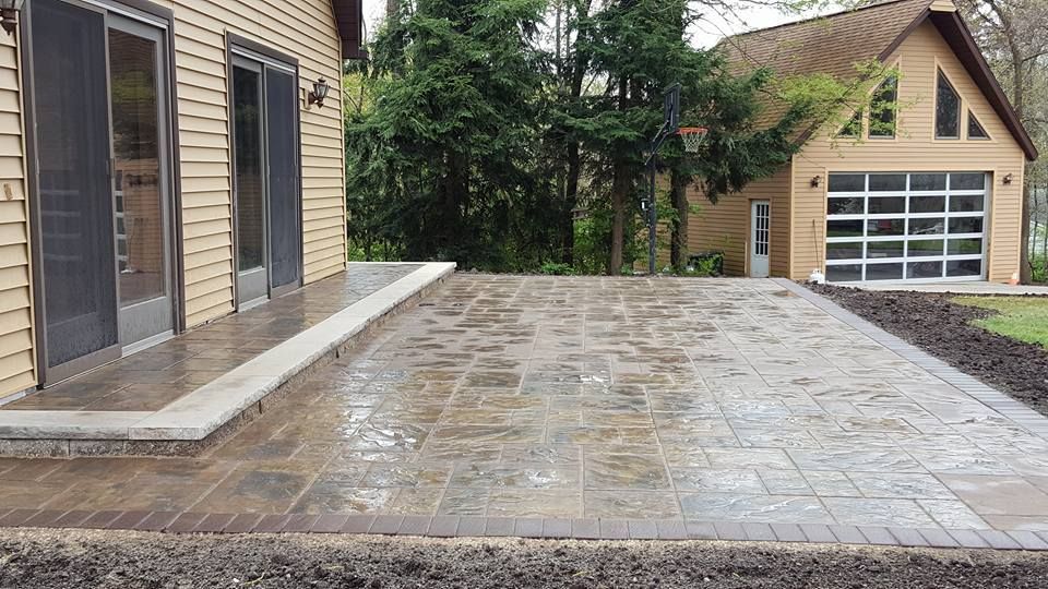 Patio with wet brick pavers, bordering a house with glass doors and a detached garage.