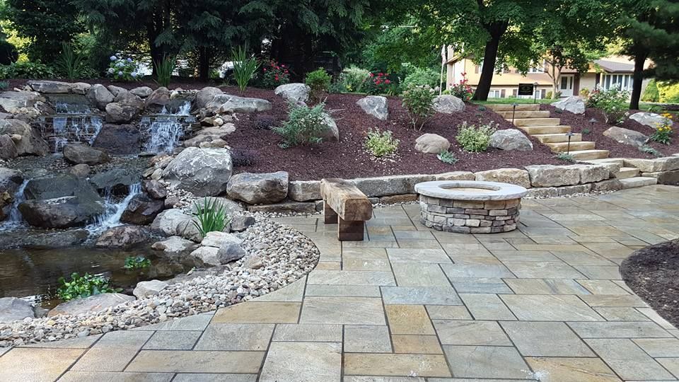 Stone patio with waterfall, fire pit, and landscaping.
