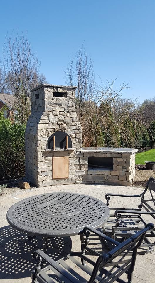 Stone pizza oven with a table and chairs on a patio, blue sky.