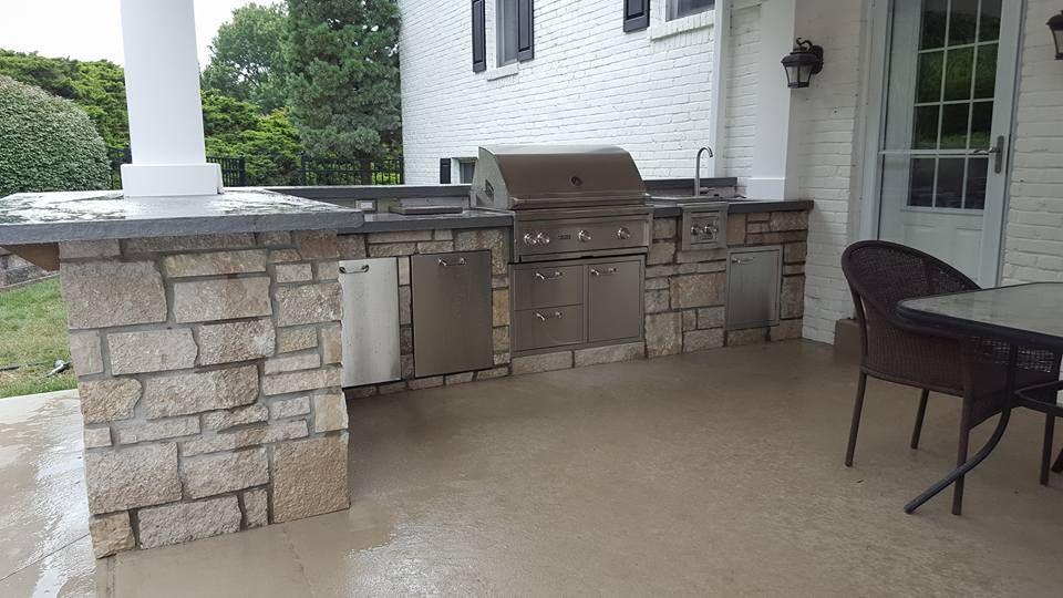 Outdoor kitchen with stone facade, stainless steel grill, and cabinets.