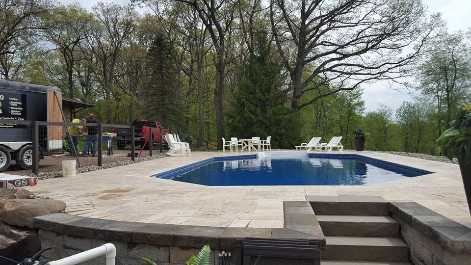 Swimming pool with stone patio, surrounded by trees.
