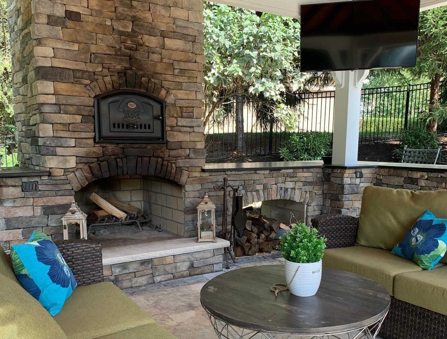 Outdoor patio with stone fireplace and pizza oven, seating area, and a TV.