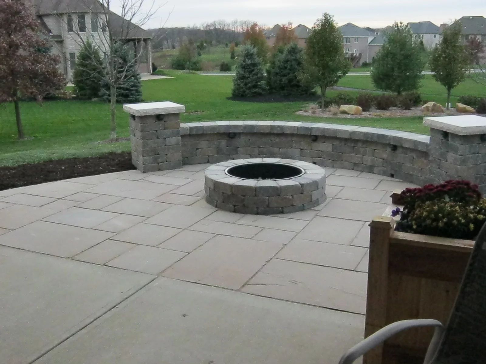 Stone patio with fire pit and seating wall, grassy backyard.