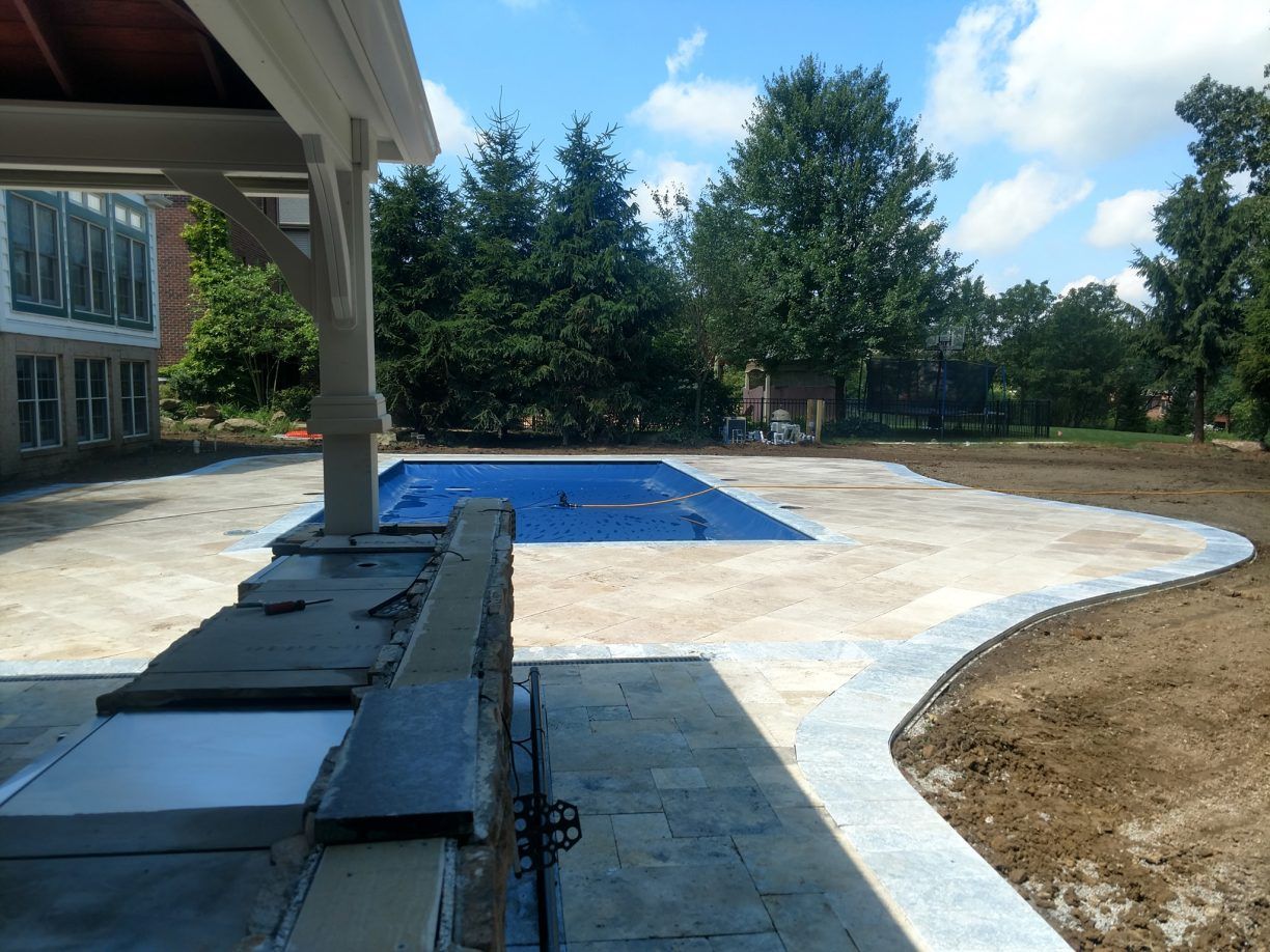 Backyard with pool, patio, and outdoor kitchen, under blue sky.