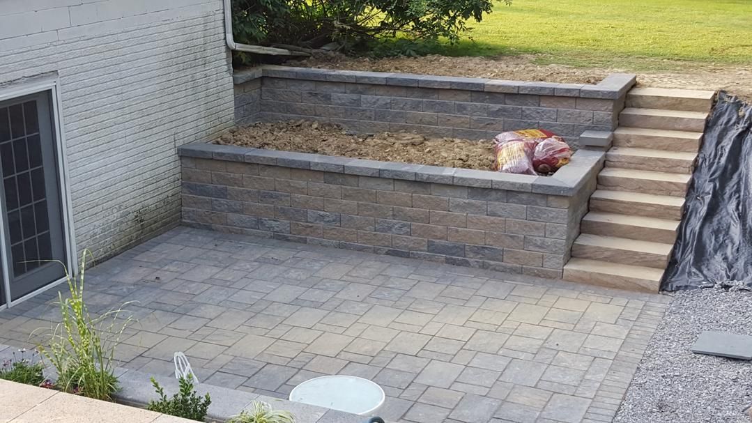 Patio with brick retaining walls, steps, and landscaping next to a house with a sliding glass door.