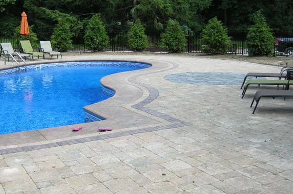 Pool area with blue water, light-colored patio, lounge chairs, and trees in the background.