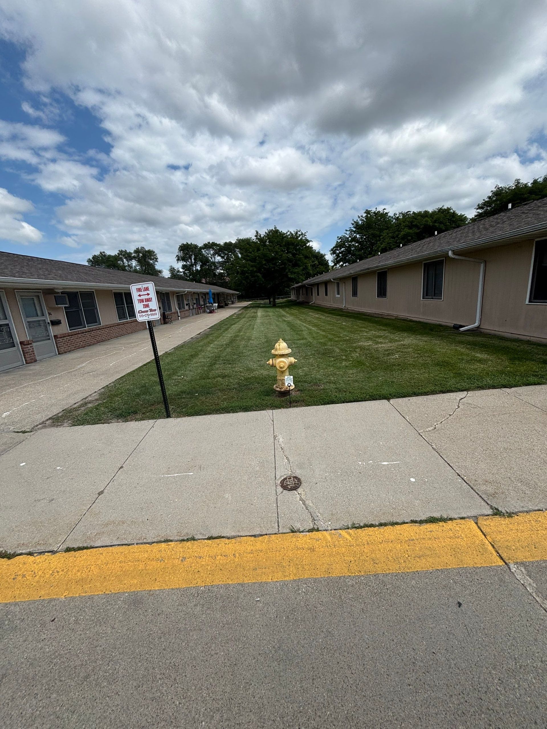 Apartment walkway with yellow curb, grassy median, fire hydrant, and cloudy sky