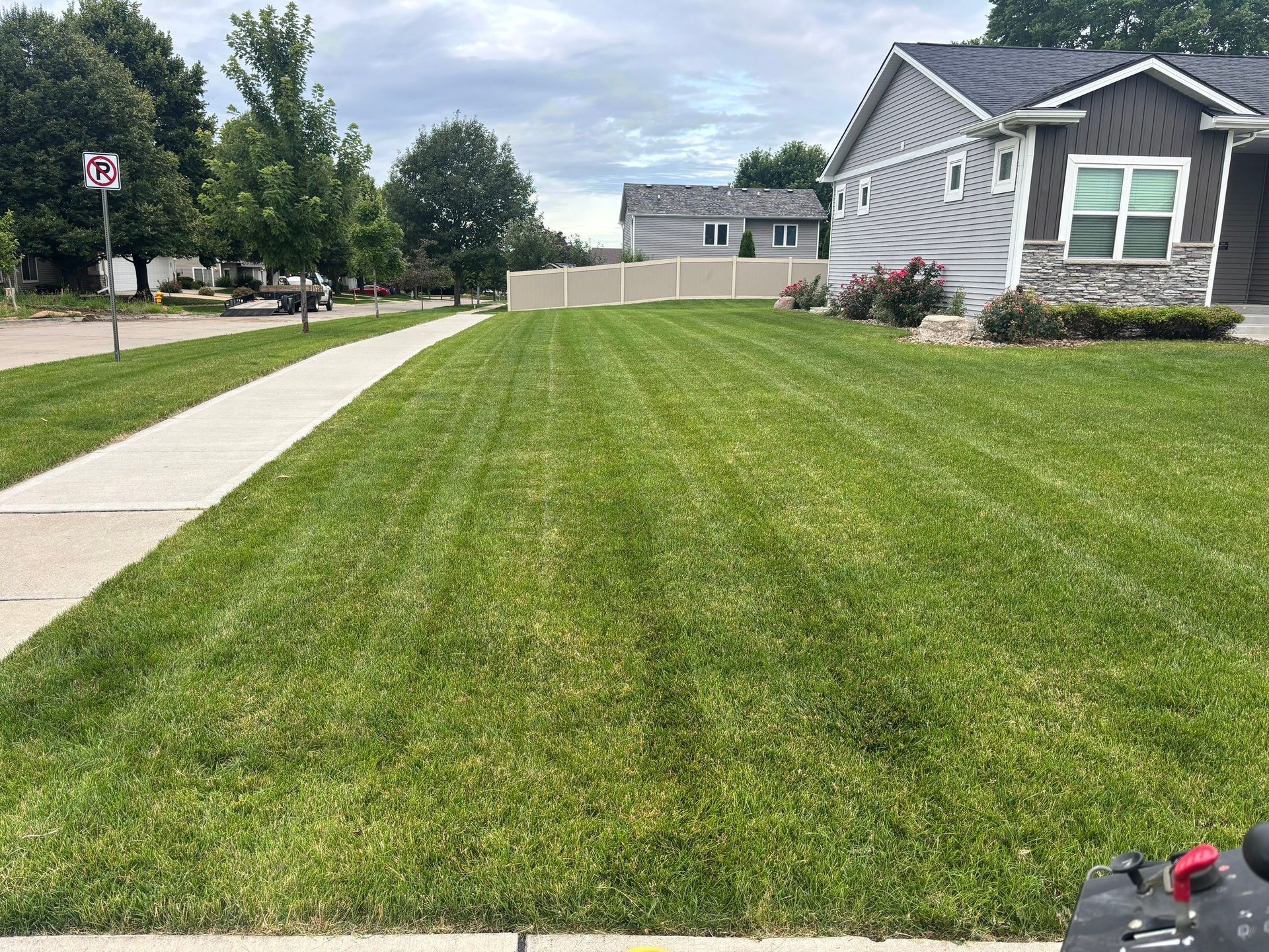 Suburban front lawn with a sidewalk, house, and green grass under a cloudy sky