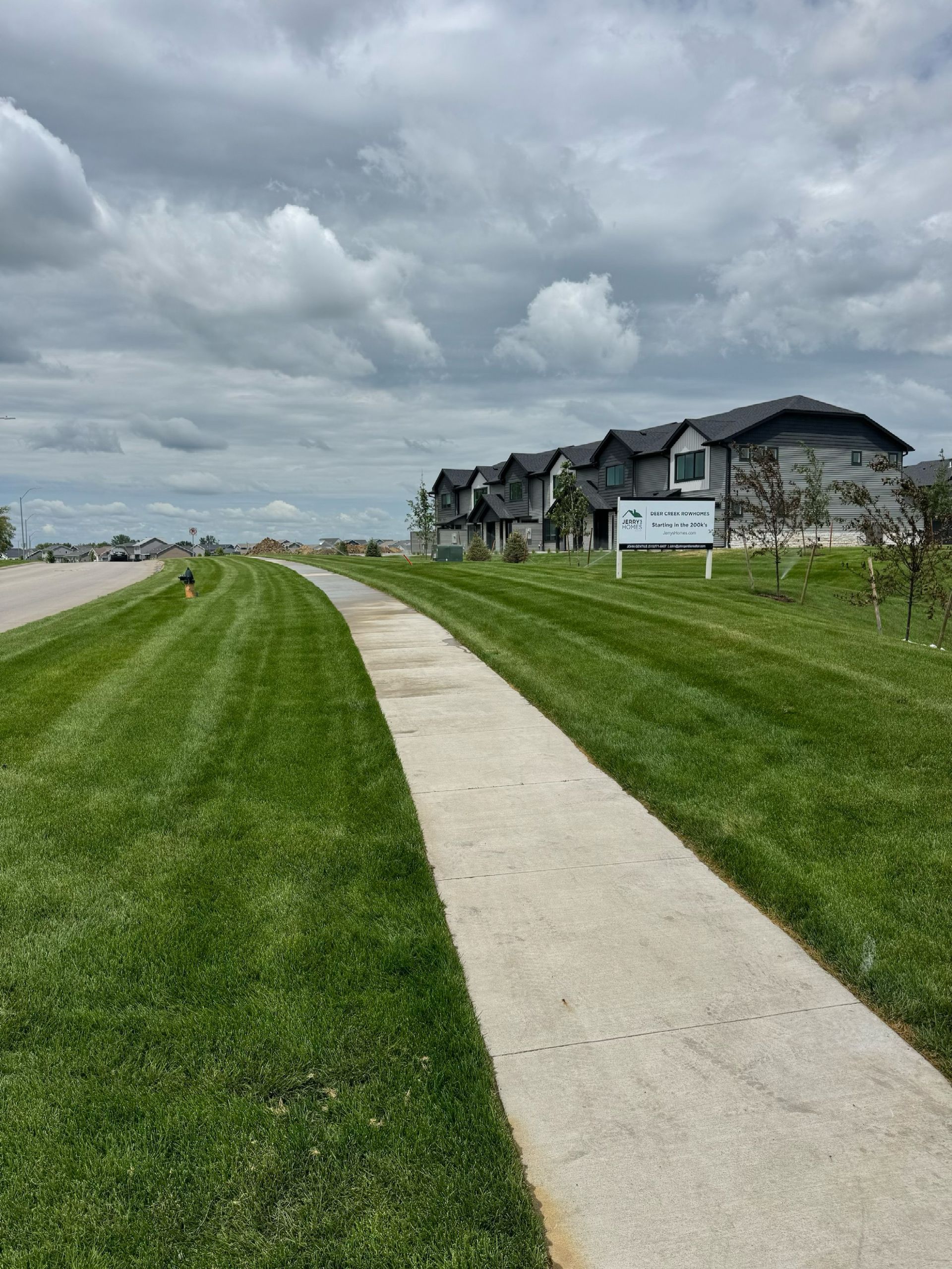 Curved sidewalk through green grass beside apartment buildings under a cloudy sky
