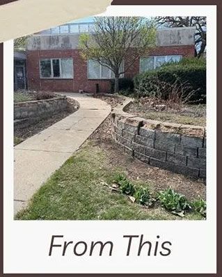 Exterior view of a building with a walkway, low stone retaining walls, and landscaping with bare spring trees.