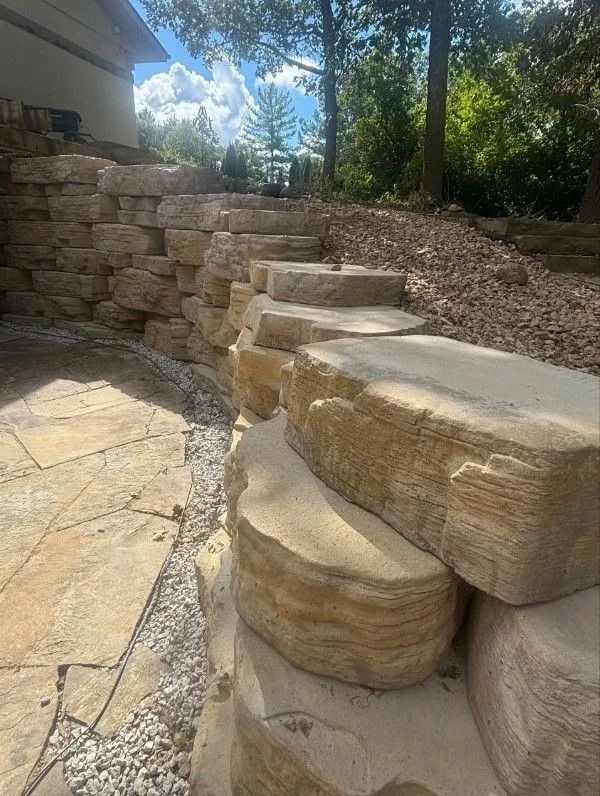 Stone steps and retaining wall leading uphill; tan stone, wood chips, and trees.