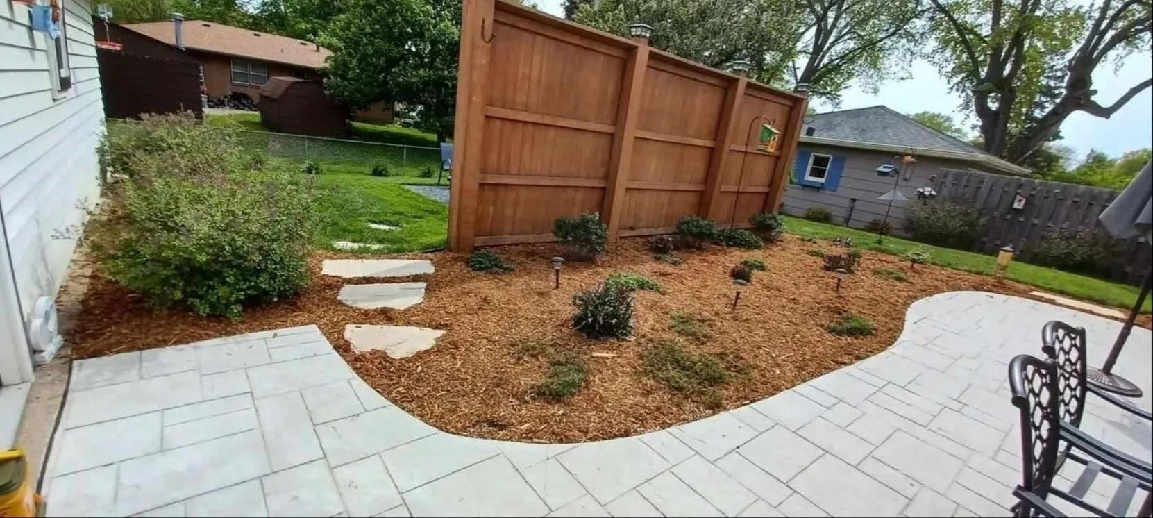 Backyard patio with wooden fence, mulch, and stone path.