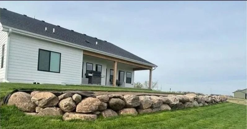 White house with black trim and a rock retaining wall along the green lawn.