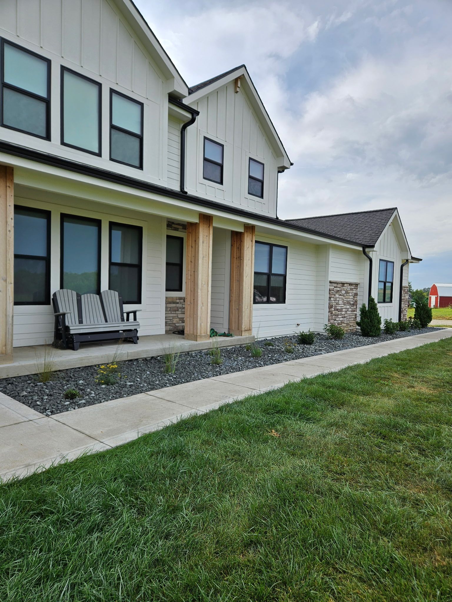 White farmhouse with black trim, gray walkway, and green lawn. Cloudy sky.